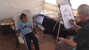 Bowie Klingonsmith, 4, sits while Oklahoma City artist Patrick Riley draws his portrait at the St. George Art Festival, St. George, Utah, April 3, 2015 | Photo by Holly Coombs, St. George News