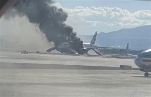 In this photo, taken from the view of a plane window, smoke billows out from an airplane that caught fire at McCarran International Airport. An engine on the British Airways plane caught fire before takeoff, forcing passengers to escape on emergency slides. Las Vegas, Nevada, Sept. 8, 2015 | AP Photo by Eric Hays, St. George News