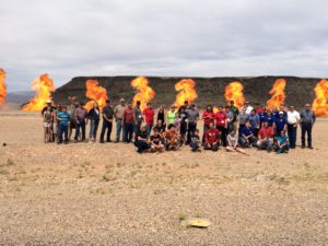 Participants of a mass casualty drill organized by the Utah Association of Emergency Technicians line up for a group photo while fireballs explode behind them. St. George, Utah, May 20, 2016 | Photo by Don Gilman, St. George News
