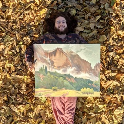 Artist Steven Anzardo lays on fall leaves holding one of his paintings, Location and Date Unspecified | Photo courtesy of Steven Anzardo, St. George News