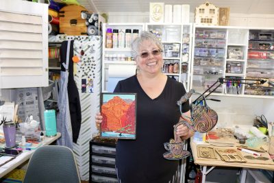 Susan Taylor stands inside her workshop holding her laser art, St. George, Utah, June 15, 2022 | Photo by Jessi Bang, St. George News