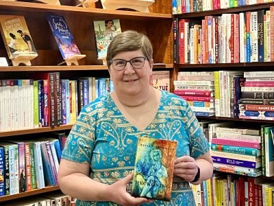 Tanya Mills stands with one of her published books inside her independent bookstore, St. George, Utah, July 27, 2022 | Photo by Jessi Bang, St. George News