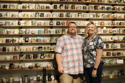 Husband and wife Joe and Emilee Bott smile in front of their personal mug collection inside The Tilted Kiln in St. George, Utah, Oct. 5, 2023 | Photo by Jessi Bang, St. George News